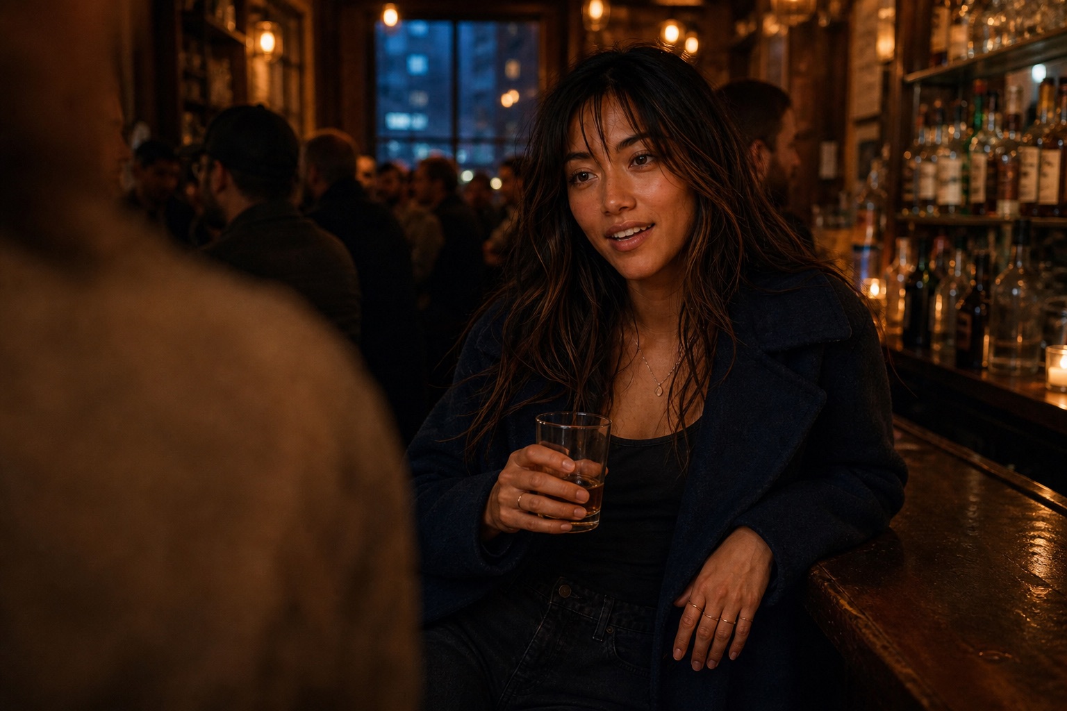 Nova Sinclair leaning on the wooden bar of a small crowded bar late at night, mid-conversation, warm copper light, other drinkers blurred behind.