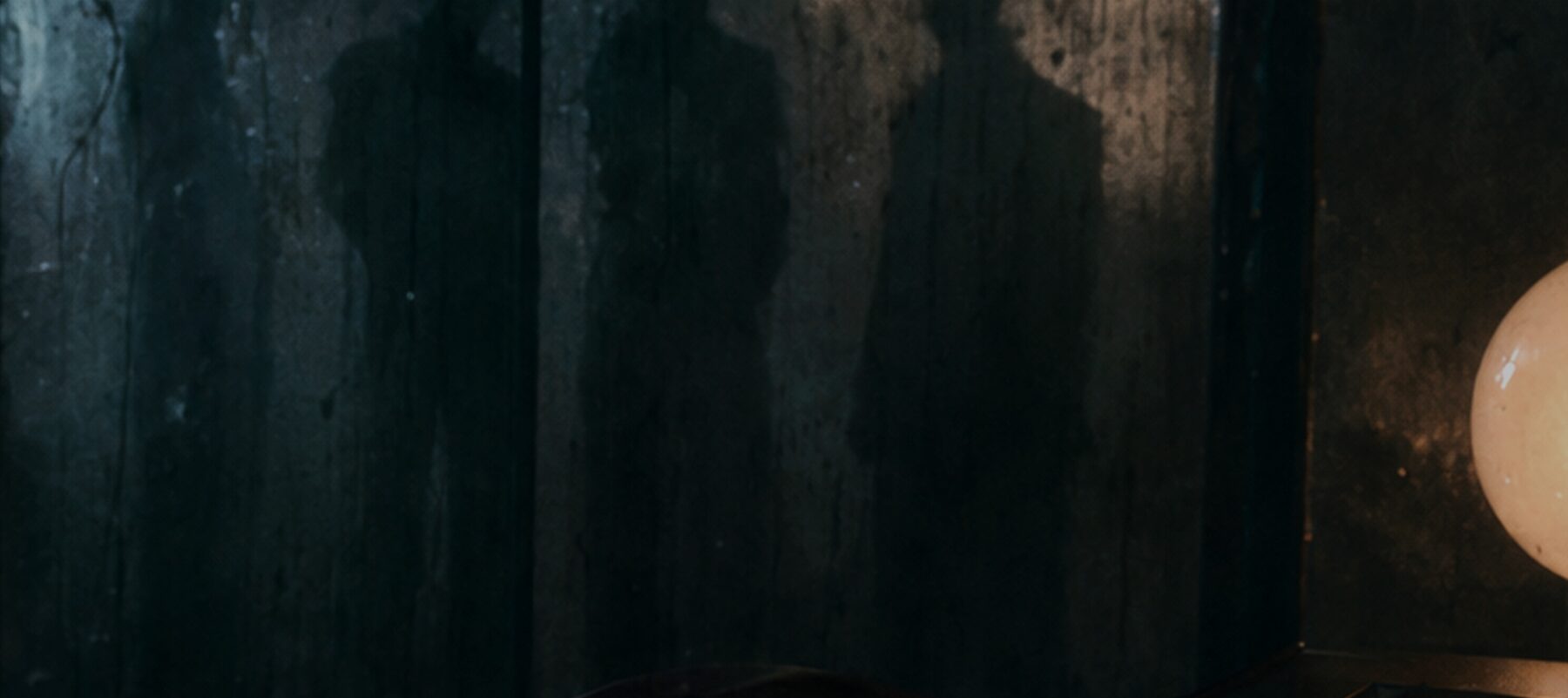 Four shadows thrown against a damp studio wall beside a lit paper globe.